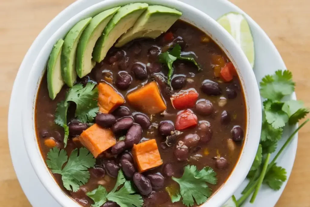 A steaming bowl of purple black bean soup garnished with fresh cilantro, avocado slices, served in a rustic bowl.